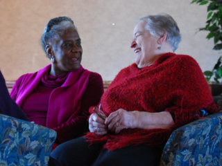 A woman in a purple shirt and a woman in a red shirt sit together, talking and laughing.