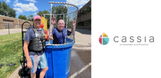 Cassia President and CEO Bob Dahl stands smiling next to a dunk tank, wearing a life jacket, while another Cassia employee sits inside the dunk tank during a sunny State Fair-inspired picnic event.