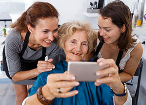 Senior woman smiling while taking a selfie with two stylists at a beauty salon.