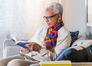 Senior woman reading a book while relaxing in a cozy common space.