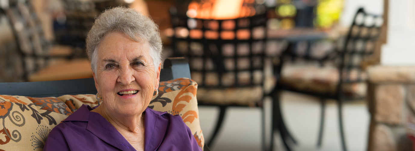 Carol, a generous donor, sitting outdoors on a cushioned chair, smiling warmly.