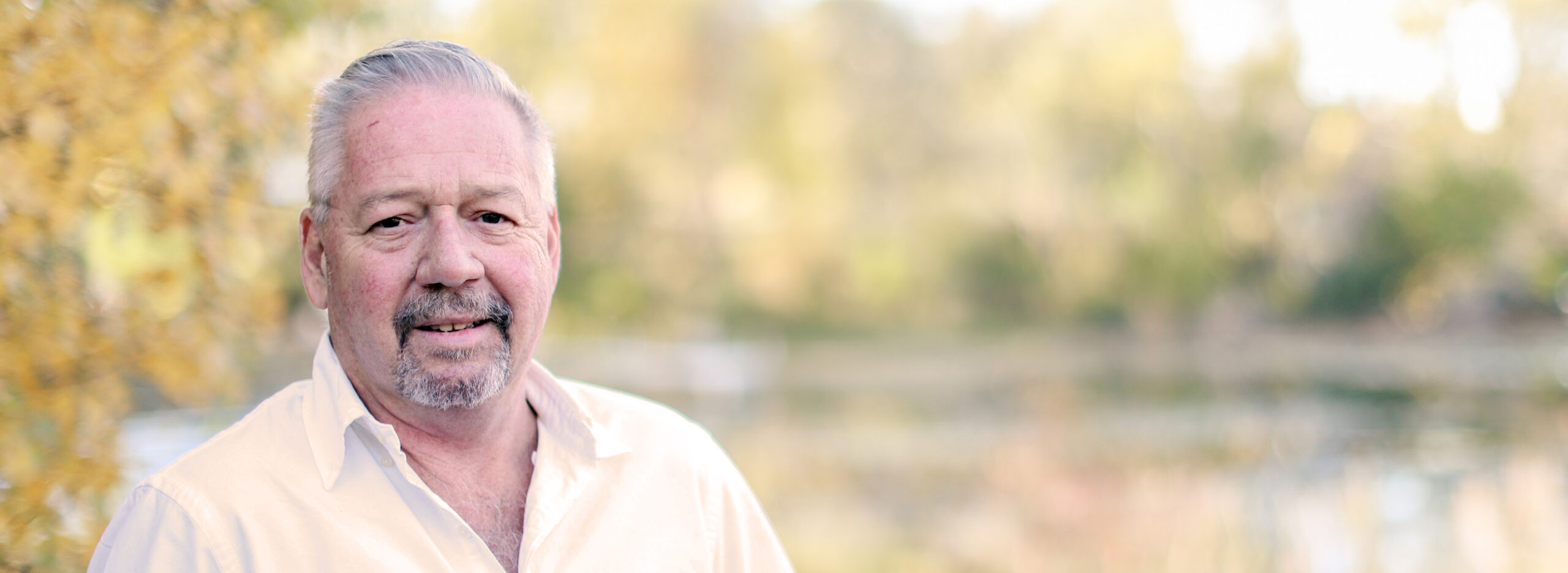 Dave smiles outdoors with a blurred yellow landscape in the background.
