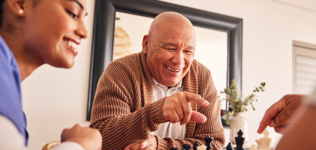 Senior enjoying a chess game with a caregiver, highlighting connection and independence in a familiar community setting.