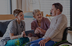 Adult in a wheelchair speaking with two others in a home-like setting, representing compassionate care and support through donations at Cassia