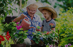 Older adult and child watering flowers together in a garden setting, representing opportunities for residents to experience nature and enjoy the outdoors at Cassia