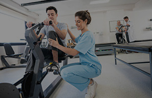 Adult using exercise equipment with assistance from a staff member in a rehabilitation space, representing investment in modern care tools and technology at Cassia