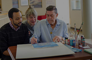 Three adults seated at a table painting together with art supplies in a creative activity setting, representing opportunities for residents to explore interests and stay engaged at Cassia