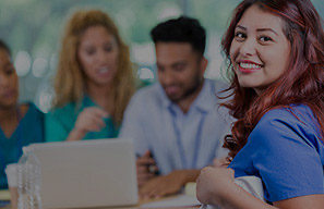 Adult seated at a table with coworkers using a laptop in a collaborative setting, representing staff development and resources that support high-quality care at Cassia