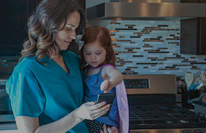Adult holding a small child while looking at a phone in a home setting, representing support for staff members facing financial challenges at Cassia