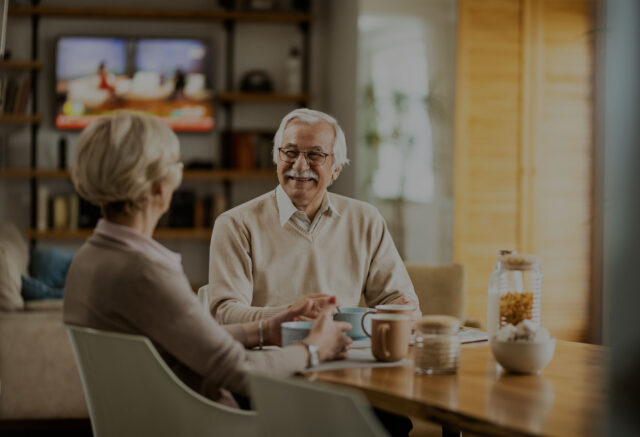 Two seniors enjoying coffee and conversation in a cozy kitchen setting, representing independent living lifestyle like The Pines of Richfield in Richfield, Minnesota