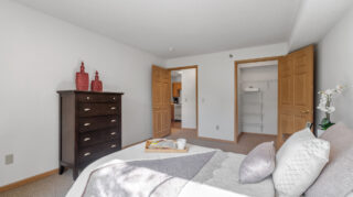 Bedroom with bed, dresser, and open closet space leading toward a kitchenette area at The Pines of Richfield in Richfield, Minnesota