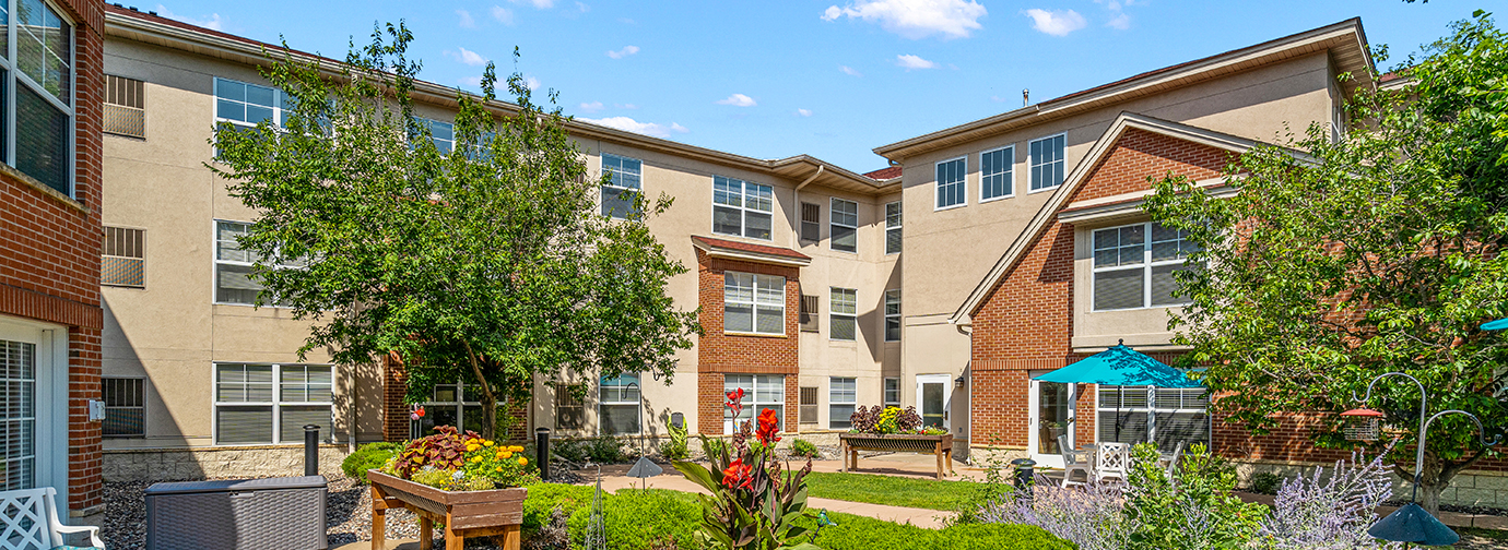 Courtyard garden with walking paths, raised flower beds, and outdoor seating at The Pines of Richfield senior living community in Richfield, Minnesota