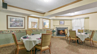 Dining room with tables, chairs, fireplace, and place settings in a comfortable community setting at The Pines of Richfield in Richfield, Minnesota