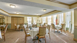 Spacious dining room with tables, chairs, large windows, and place settings in a bright community space at The Pines of Richfield in Richfield, Minnesota