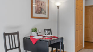 Small dining table for two with chairs, place settings, and wall decor in a comfortable apartment space at The Pines of Richfield in Richfield, Minnesota