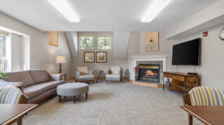 Comfortable lounge with sofa, chairs, fireplace, and television in a spacious common area at The Pines of Richfield in Richfield, Minnesota