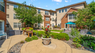 Landscaped courtyard garden with a central planter, raised flower beds, and surrounding patio seating at The Pines of Richfield in Richfield, Minnesota