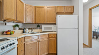 Kitchenette with wood cabinets, sink, microwave, stove, and refrigerator in an apartment at The Pines of Richfield in Richfield, Minnesota
