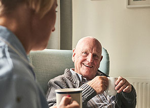 Two older adults seated in a comfortable living room setting with coffee mugs, representing social interaction like The Pines of Richfield in Richfield, Minnesota