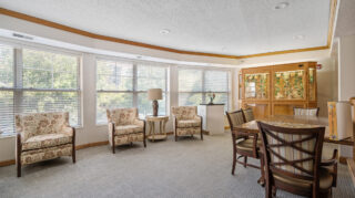 Comfortable lounge area with chairs, table, large windows, and an aviary enclosure at The Pines of Richfield in Richfield, Minnesota