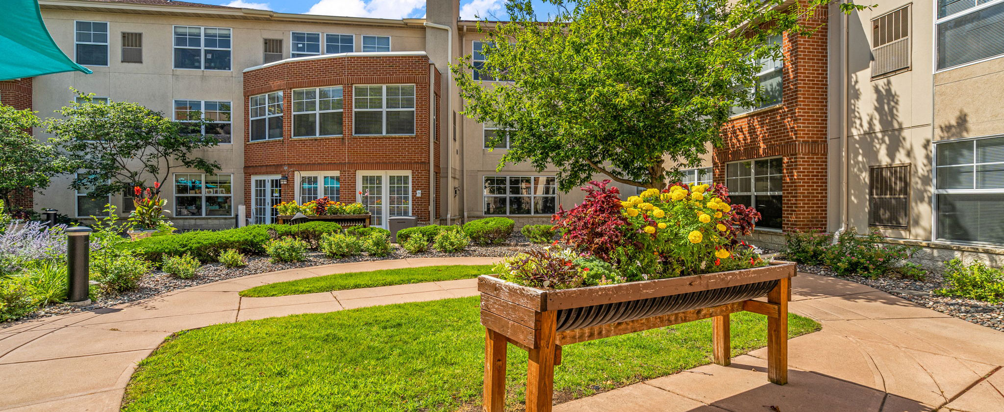 Courtyard garden with walking paths, raised flower beds, and outdoor seating at The Pines of Richfield senior living community in Richfield, Minnesota
