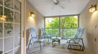 Screened-in porch with cushioned chairs, small table, and ceiling fan overlooking greenery at The Pines of Richfield in Richfield, Minnesota