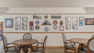 Wall of Honor display with framed military photos, service emblems, and American flag elements above seating area at The Pines of Richfield in Richfield, Minnesota