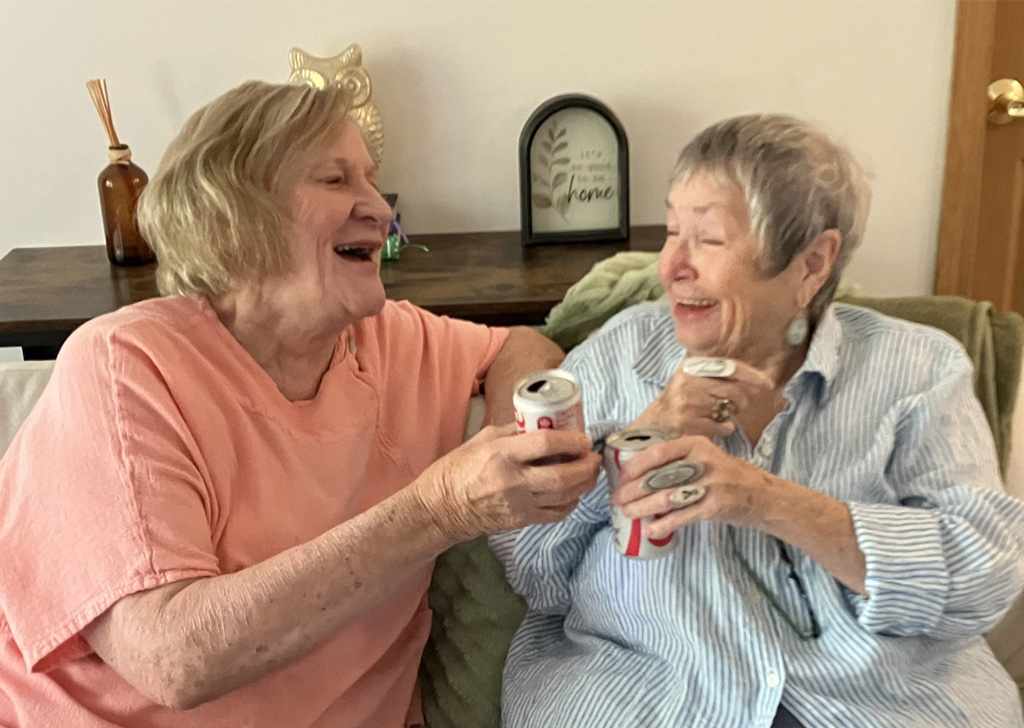 Two people sitting on a couch, holding soda cans and chatting in a cozy living room.