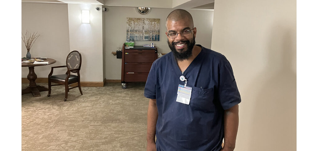 Person in navy scrubs standing in a hallway of a senior living community.